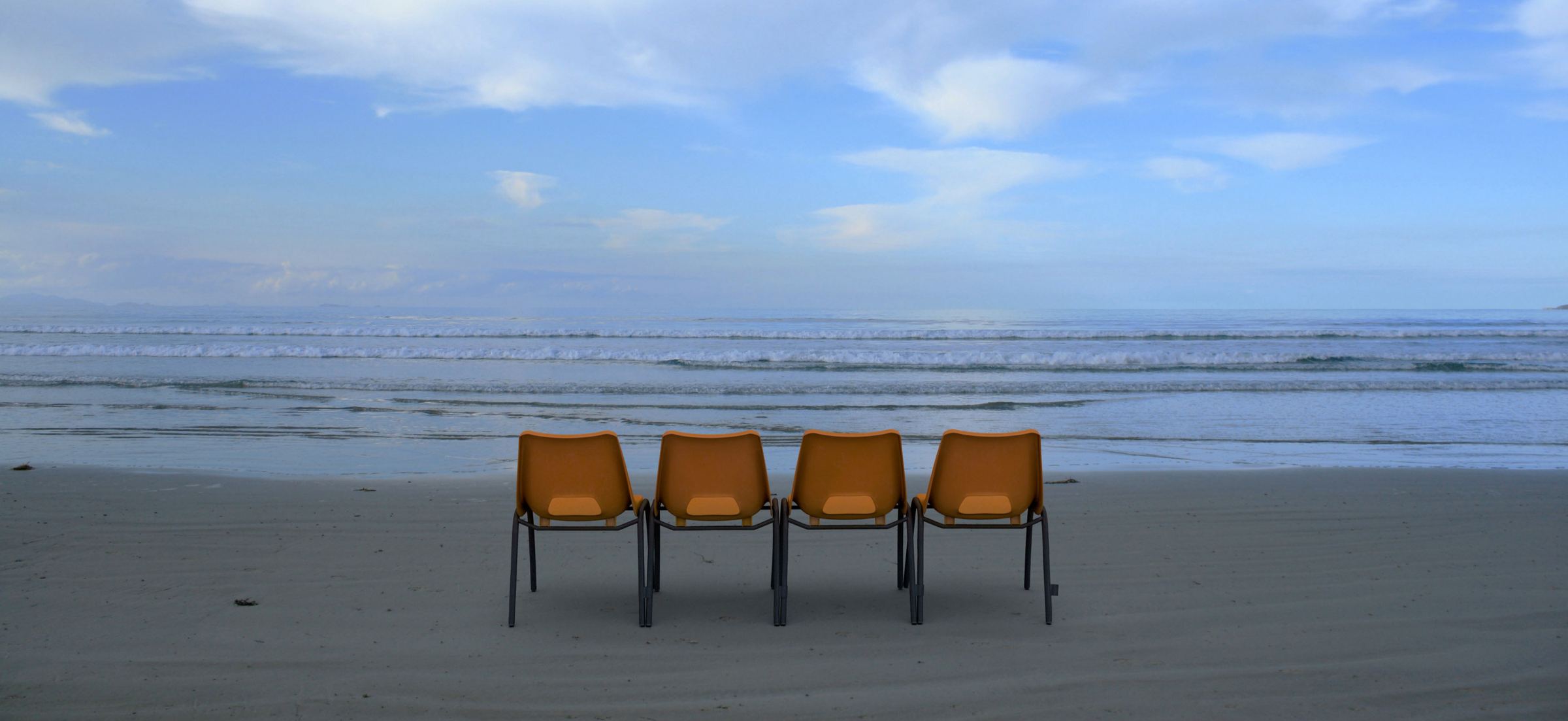 Four orange chairs in a row on a beach